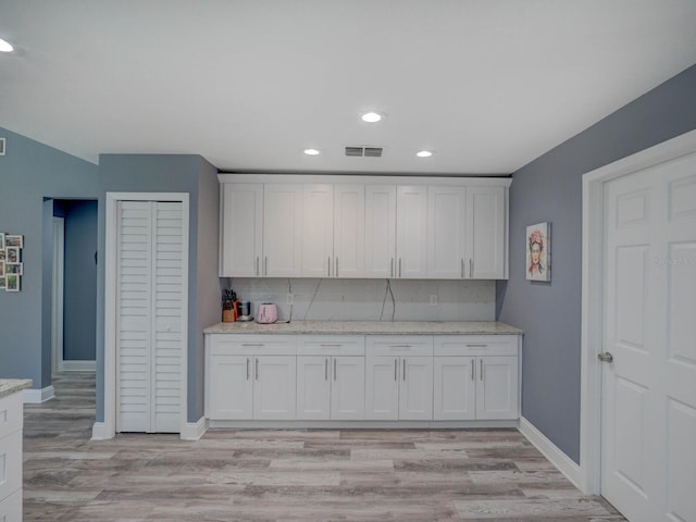 kitchen with decorative backsplash, light wood-style floors, white cabinets, light stone countertops, and baseboards