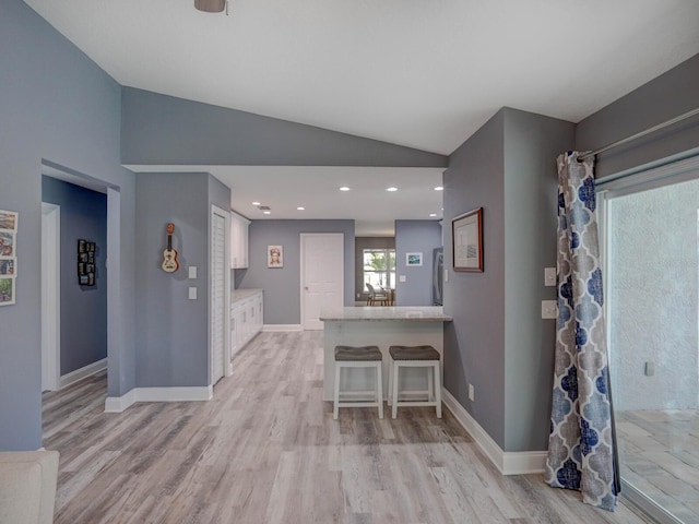 kitchen with a breakfast bar, lofted ceiling, light countertops, white cabinets, and baseboards