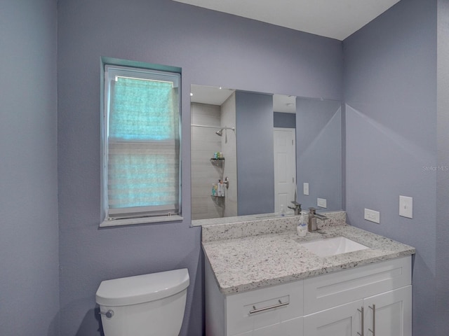 bathroom with toilet, a tile shower, and vanity