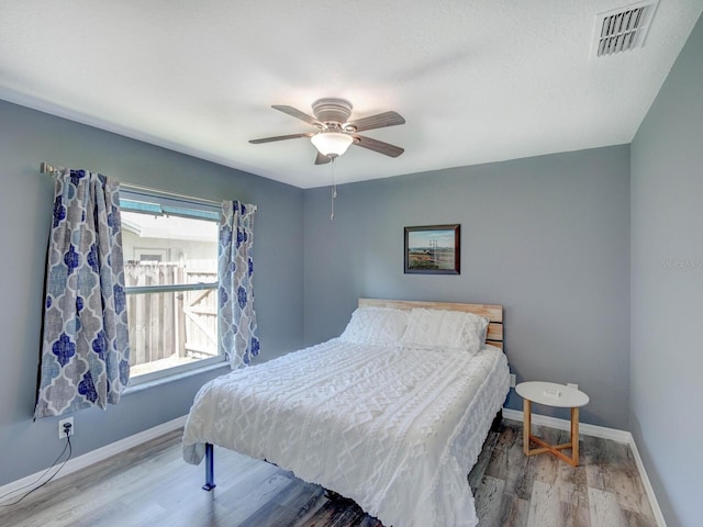 bedroom with a ceiling fan, baseboards, visible vents, and wood finished floors