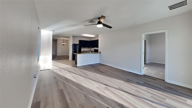 interior space with visible vents, baseboards, light wood-style floors, and ceiling fan with notable chandelier