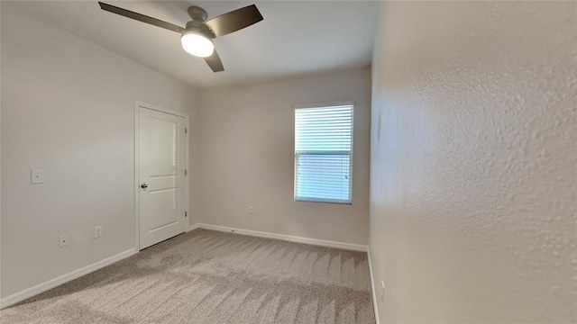 carpeted spare room with a ceiling fan and baseboards