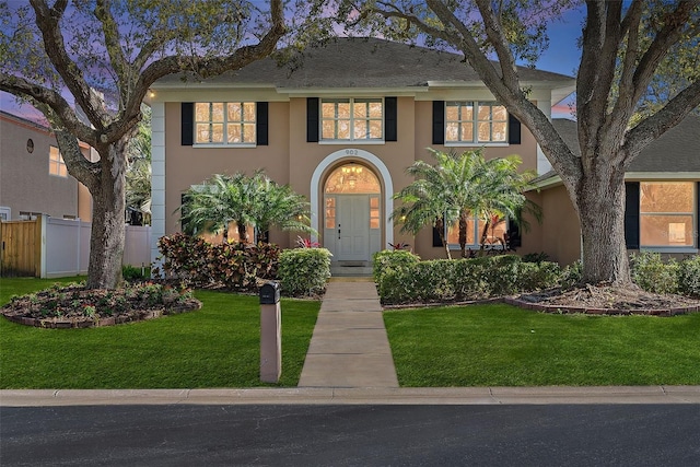 view of front facade with stucco siding, a front yard, and fence