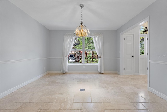 spare room featuring stone tile flooring, baseboards, and a chandelier