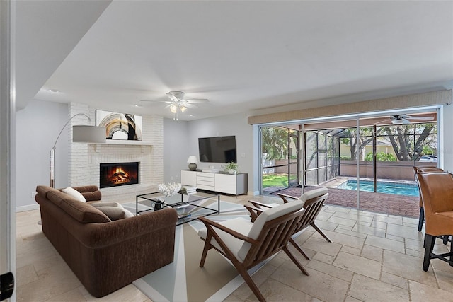 living room with a brick fireplace, baseboards, a sunroom, stone tile flooring, and a ceiling fan