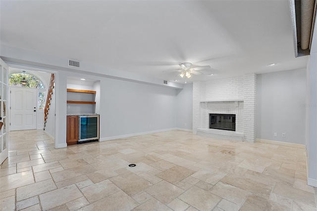 unfurnished living room with visible vents, stone tile flooring, wine cooler, baseboards, and a brick fireplace