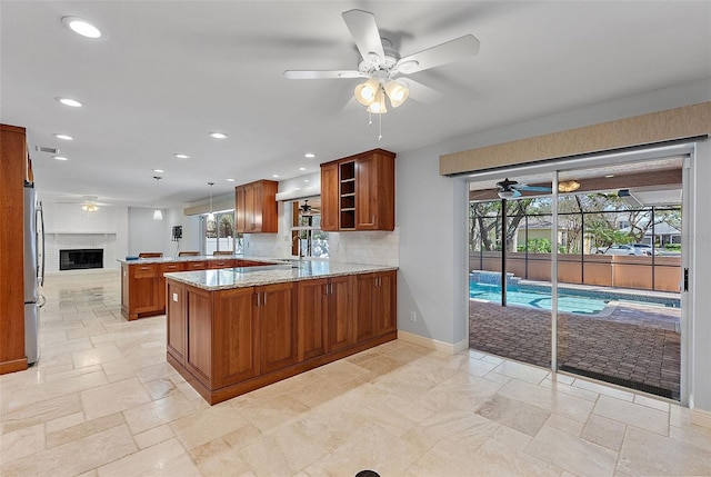 kitchen with brown cabinets, stone tile flooring, freestanding refrigerator, a peninsula, and light stone countertops