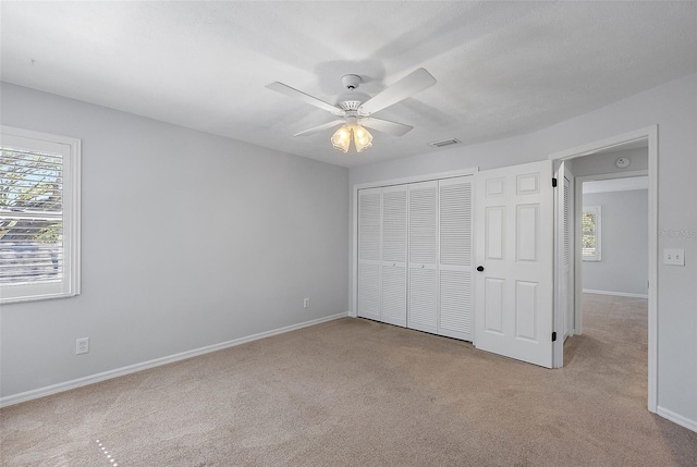 unfurnished bedroom featuring visible vents, multiple windows, carpet floors, and a closet