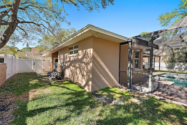 exterior space with stucco siding, glass enclosure, a fenced backyard, and a gate