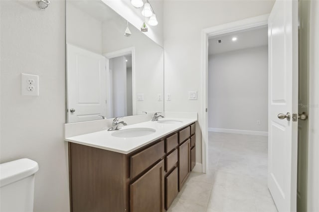 bathroom with toilet, double vanity, baseboards, and a sink