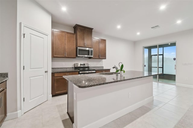 kitchen featuring visible vents, dark stone counters, an island with sink, stainless steel appliances, and a sink