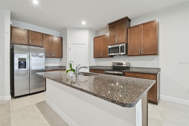 kitchen featuring a center island with sink, recessed lighting, appliances with stainless steel finishes, a sink, and dark stone countertops