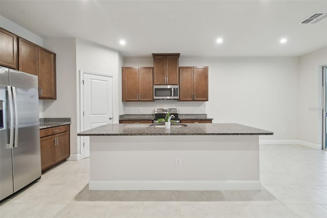 kitchen featuring a kitchen island with sink, stainless steel appliances, a sink, visible vents, and dark stone countertops