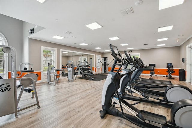 workout area with light wood-style floors, visible vents, and ornamental molding