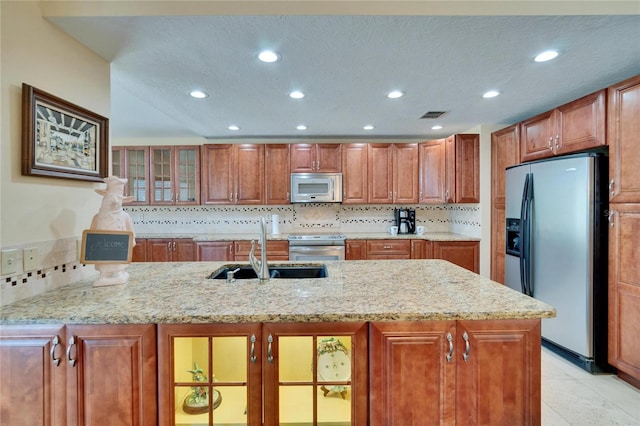 kitchen featuring stainless steel appliances, a sink, visible vents, brown cabinetry, and glass insert cabinets