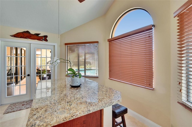 kitchen with light stone counters, french doors, lofted ceiling, baseboards, and a kitchen breakfast bar