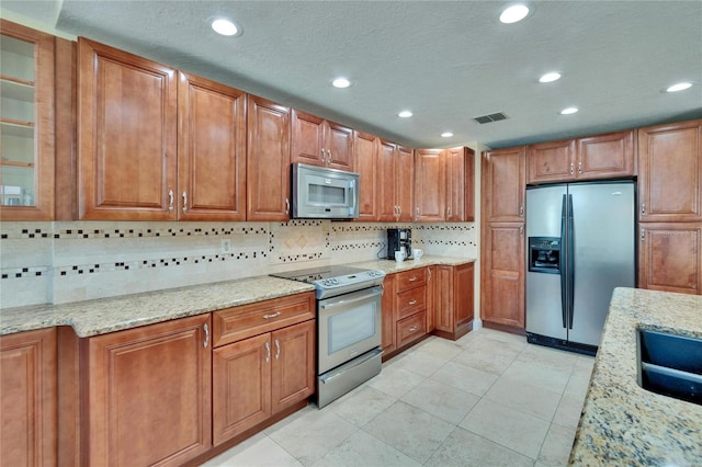 kitchen featuring appliances with stainless steel finishes, brown cabinets, visible vents, and light stone counters