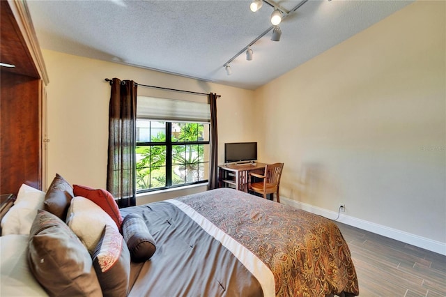 bedroom featuring a textured ceiling, ceiling fan, baseboards, dark wood-style floors, and rail lighting