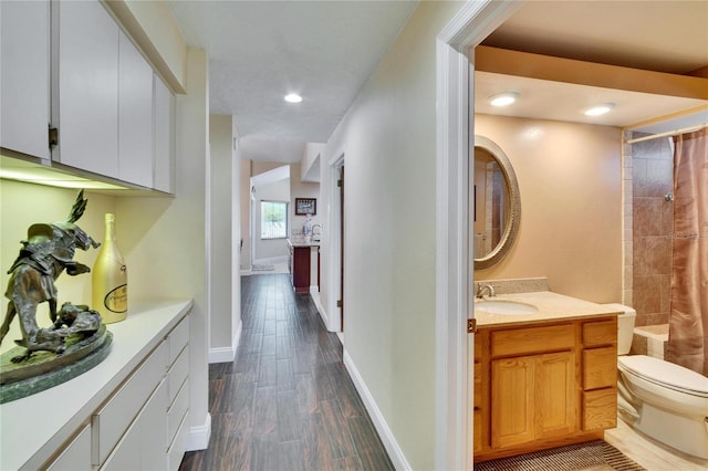 hallway featuring baseboards, dark wood finished floors, a sink, and recessed lighting