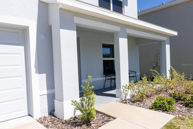 doorway to property featuring covered porch, stucco siding, and a garage