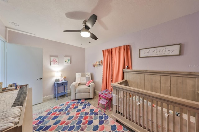 bedroom with a nursery area, a textured ceiling, baseboards, and a ceiling fan