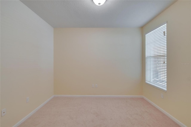 empty room featuring light carpet, a textured ceiling, and baseboards