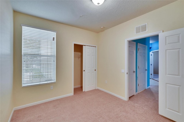 unfurnished bedroom with baseboards, visible vents, a closet, and light colored carpet