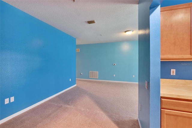 unfurnished room featuring a textured ceiling, carpet, visible vents, and baseboards