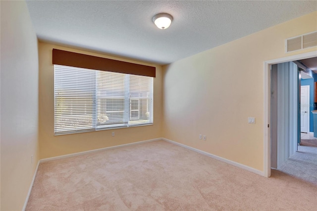 unfurnished room featuring light carpet, baseboards, visible vents, and a textured ceiling