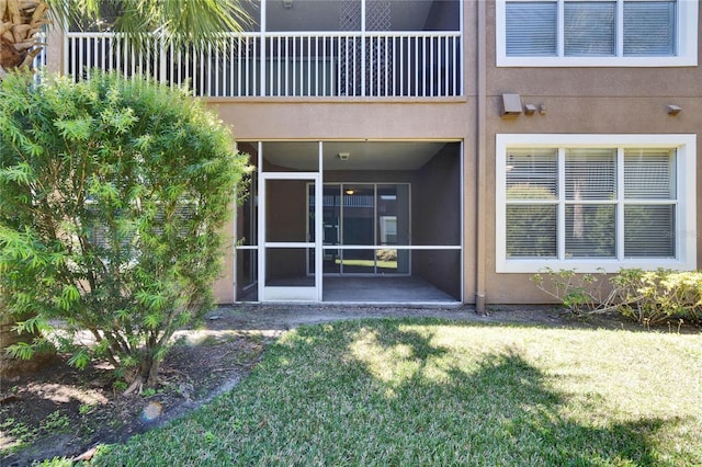 back of property with a yard, a balcony, a sunroom, and stucco siding