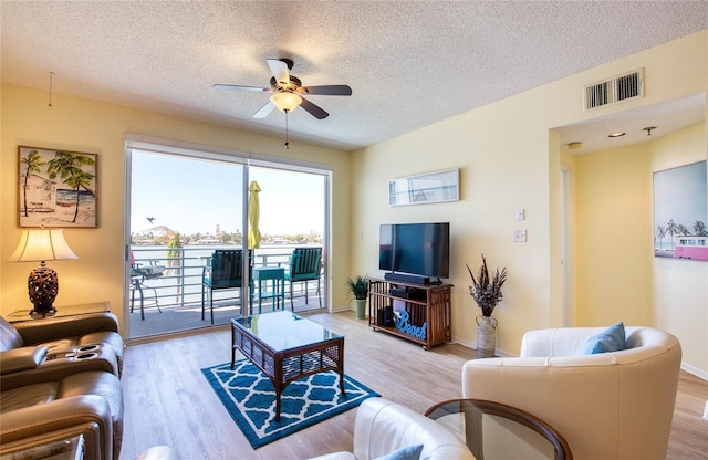 living area featuring light wood-style floors, ceiling fan, visible vents, and a textured ceiling