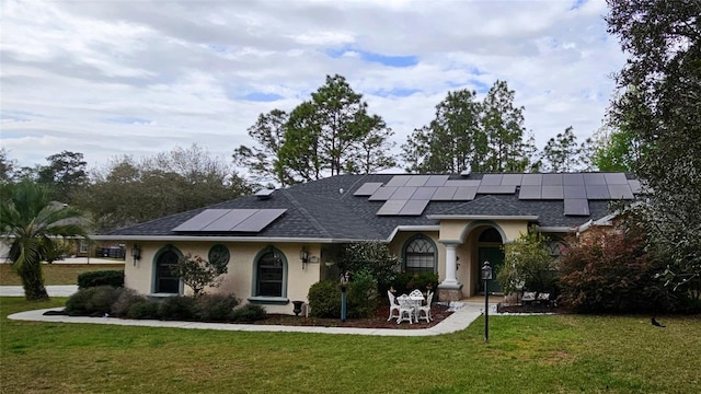 view of front facade featuring stucco siding, roof with shingles, solar panels, and a front lawn