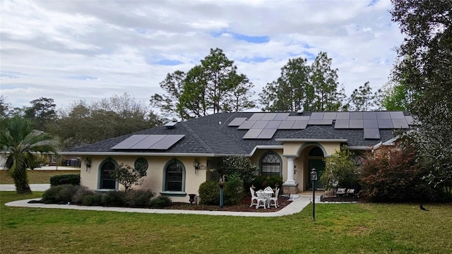 view of front facade with stucco siding, roof mounted solar panels, a front yard, and a shingled roof