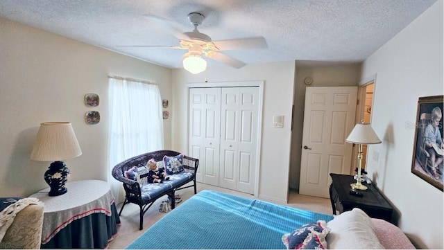 bedroom featuring a closet, light colored carpet, a textured ceiling, and a ceiling fan