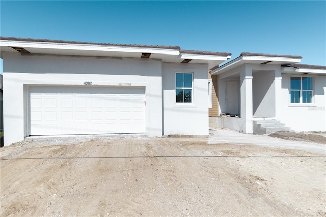 view of front of home with a garage, entry steps, dirt driveway, and stucco siding