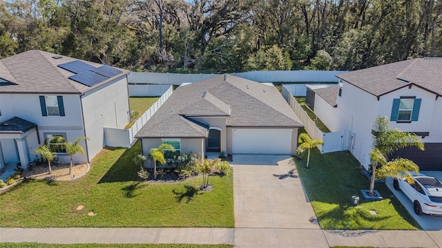 view of front facade with a fenced backyard, a garage, concrete driveway, roof with shingles, and a front lawn