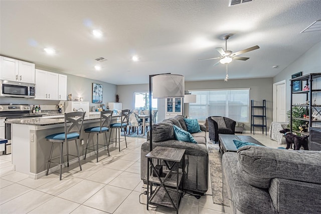 living area with light tile patterned floors, ceiling fan, a textured ceiling, and visible vents