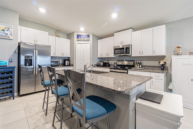 kitchen featuring light tile patterned floors, white cabinets, appliances with stainless steel finishes, a kitchen bar, and a sink