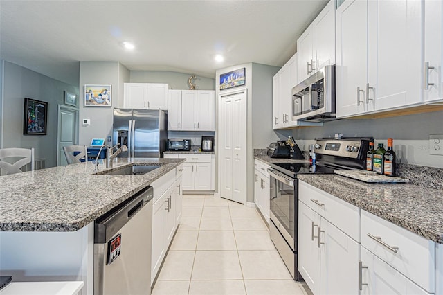 kitchen featuring light tile patterned floors, an island with sink, appliances with stainless steel finishes, dark stone countertops, and a sink