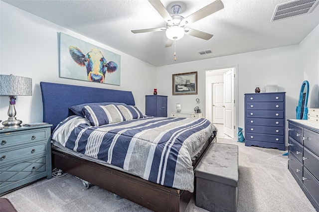 bedroom with a ceiling fan, light colored carpet, visible vents, and a textured ceiling