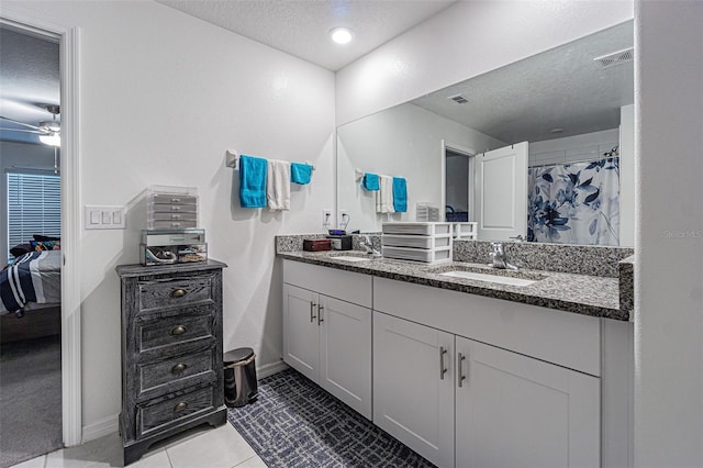 ensuite bathroom with visible vents, a sink, a textured ceiling, and double vanity