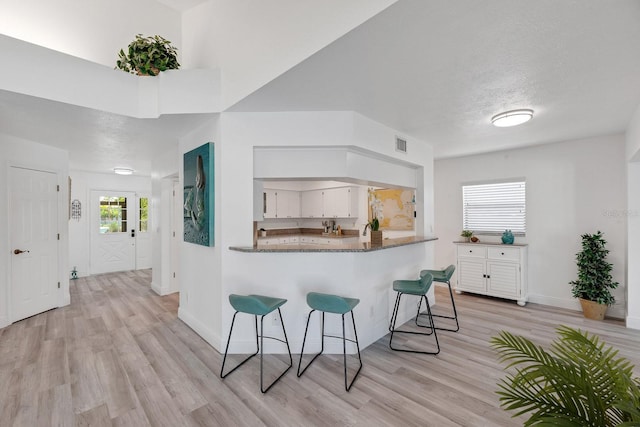 kitchen with a textured ceiling, light wood-style flooring, white cabinetry, visible vents, and a kitchen breakfast bar