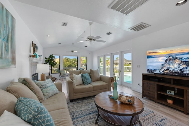 living room with vaulted ceiling, a glass covered fireplace, visible vents, and light wood-style floors