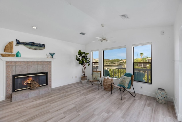 living area with a tile fireplace, wood finished floors, visible vents, baseboards, and vaulted ceiling