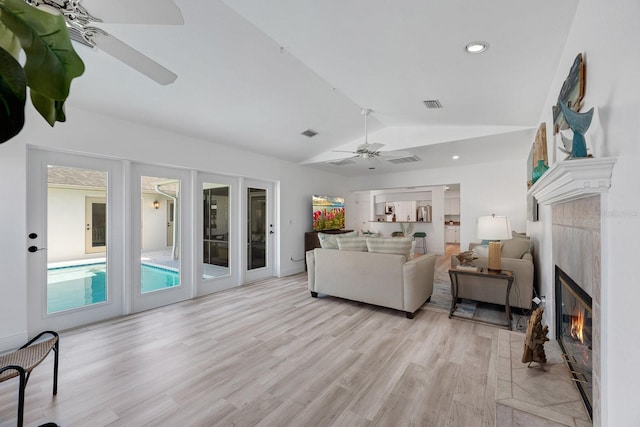 living area with visible vents, a ceiling fan, vaulted ceiling, light wood finished floors, and a tiled fireplace