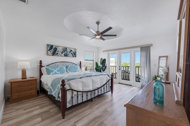 bedroom with access to outside, a tray ceiling, a textured ceiling, and light wood finished floors