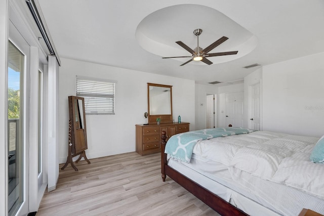 bedroom with ceiling fan, a raised ceiling, visible vents, and light wood-style floors