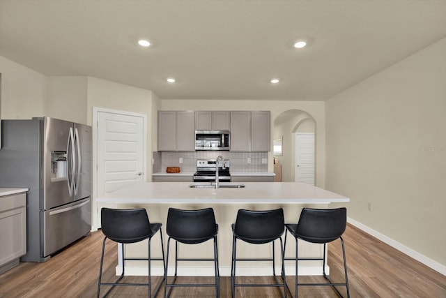 kitchen featuring arched walkways, gray cabinets, a sink, decorative backsplash, and appliances with stainless steel finishes