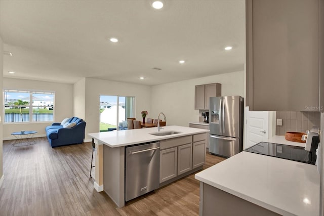 kitchen featuring a center island with sink, a sink, wood finished floors, open floor plan, and stainless steel appliances