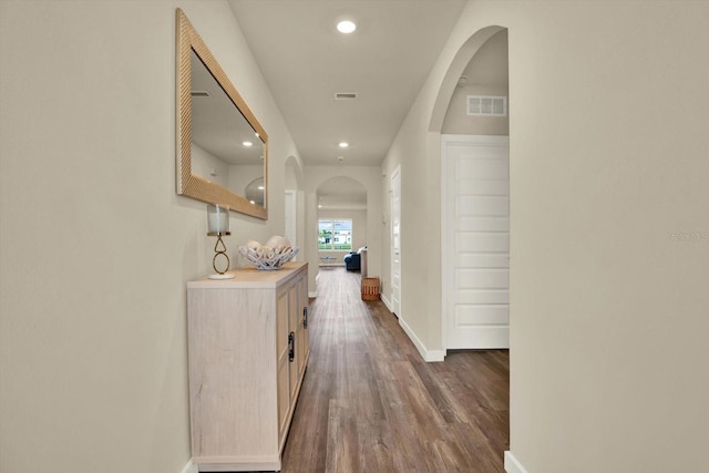 hallway with visible vents, arched walkways, baseboards, and dark wood-style flooring